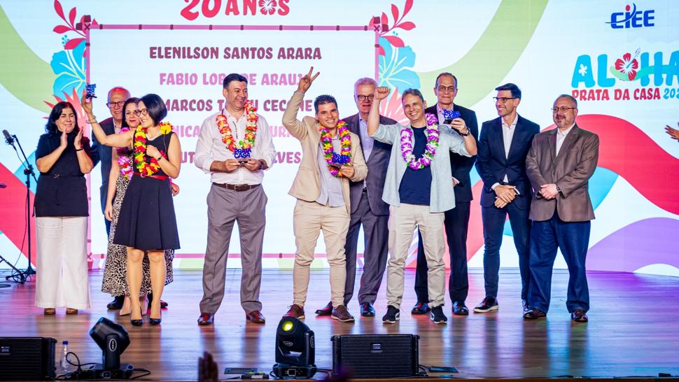 Diversas pessoas vestidas em clima Aloha em cima do palco segurando o Prêmio