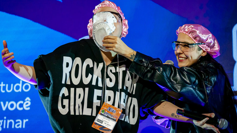 Jovem dando uma tortada na cara de um menino em cima do palco