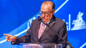 Antonio Palma, em cima do palco em um púlpito, com roupas sociais cinzas.