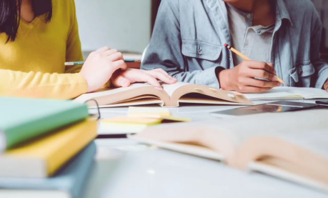 a imagem mostra duas pessoas estudando, com livros na mesa e lápis na mão