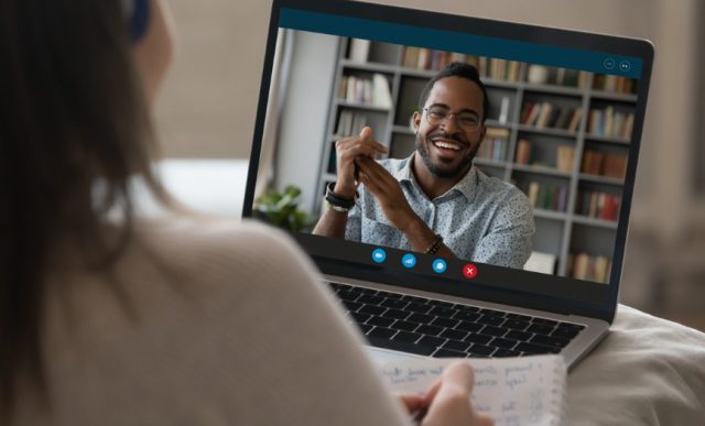 Foto de uma mulher branca sendo entrevistada, dando destaque ao notebook dela mostrando o recrutador de uma empresa em uma vídeo chamada.