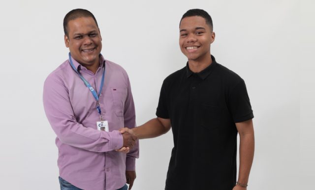 Foto com fundo cinza com dois homens sorrindo e apertando as mãos, representando um gestor dando um feedback construtivo para um estagiário.