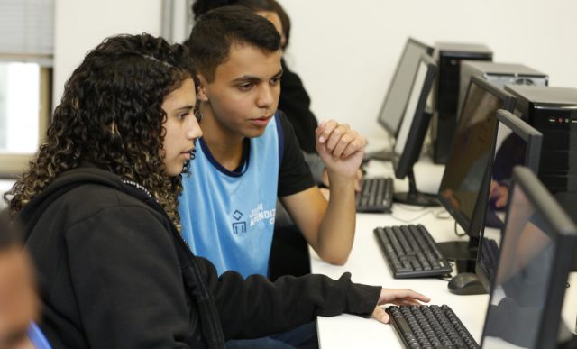 Dois estudantes sentados na frente de um computador interagindo com a tela.